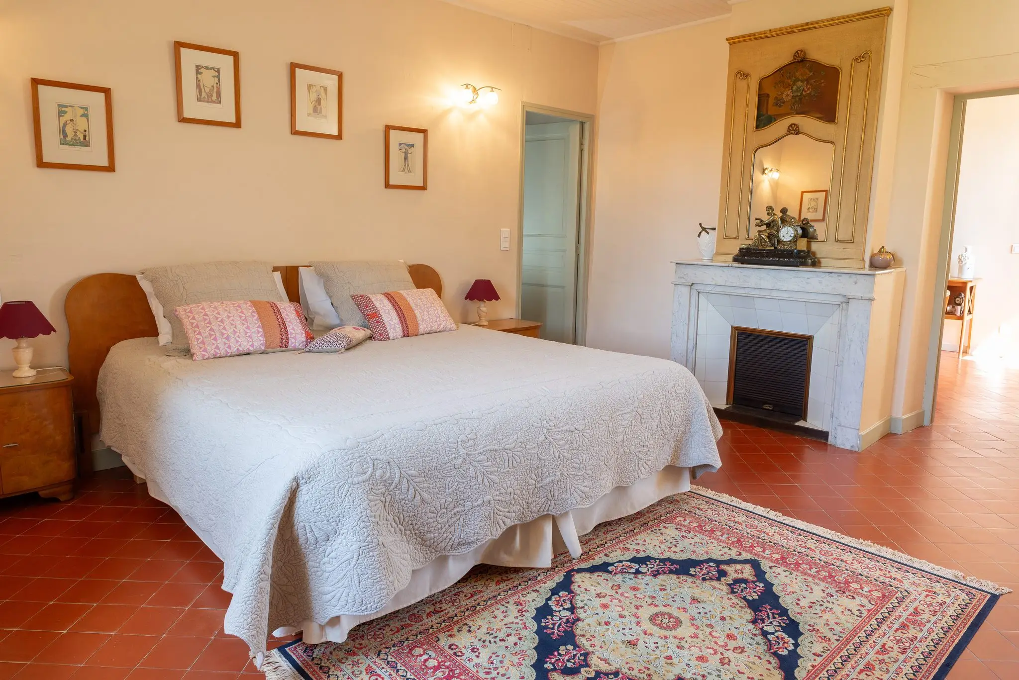 Grand lit au dessus-de-lit blanc, cheminée de marbre surmontée d'un trumeau doré, tapis d'Orient et tomettes