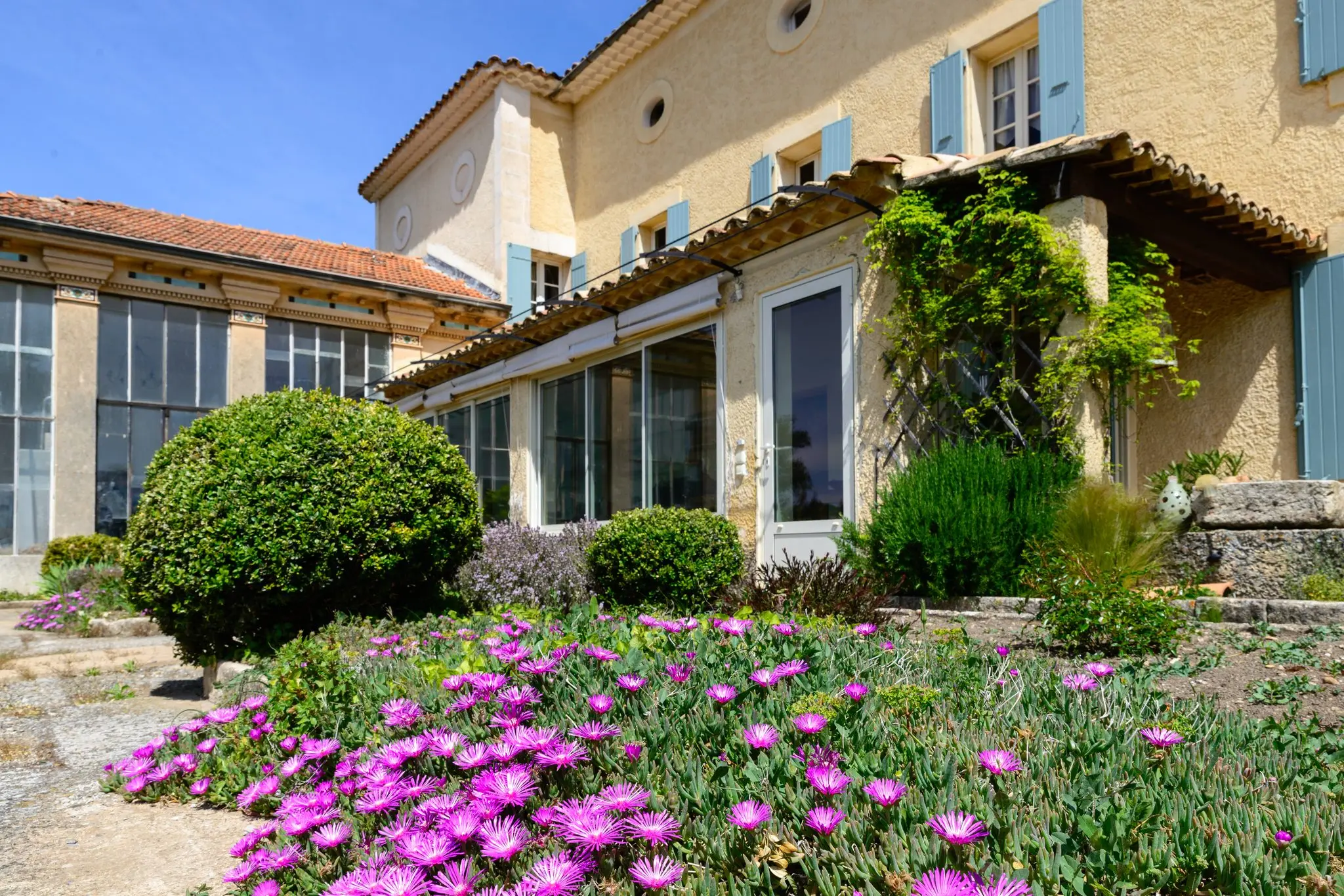 Bastide et son orangerie vitrée, massifs fleuris de rose au premier plan
