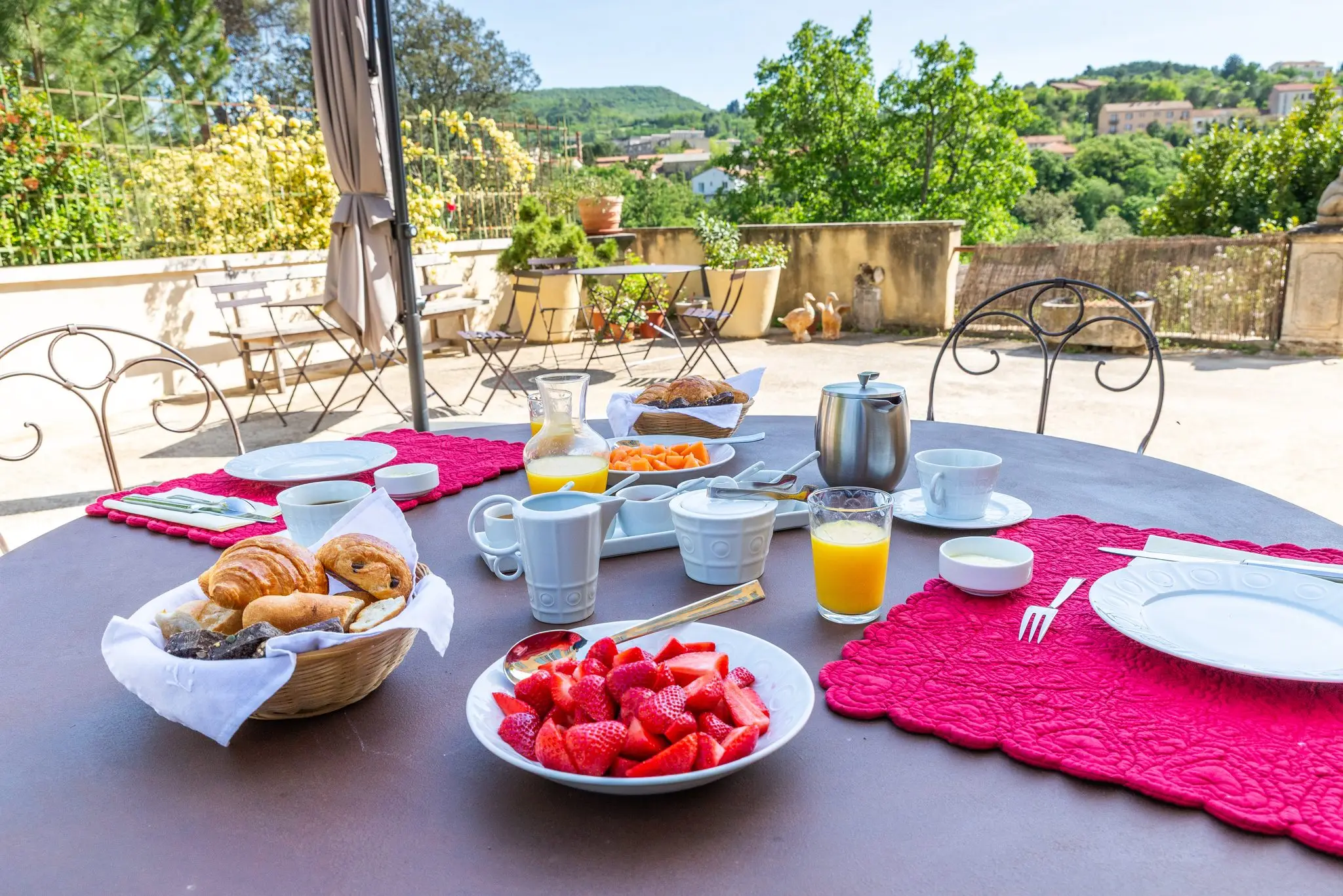 Table ronde en fer forgé dressée pour le petit-déjeuner, fraises, croissants et jus d'orange, collines en arrière-plan