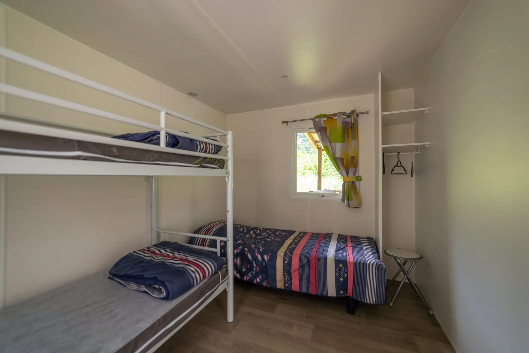 Lits superposés et lit simple aux couvre-lits rayés, penderie ouverte et fenêtre à rideau coloré