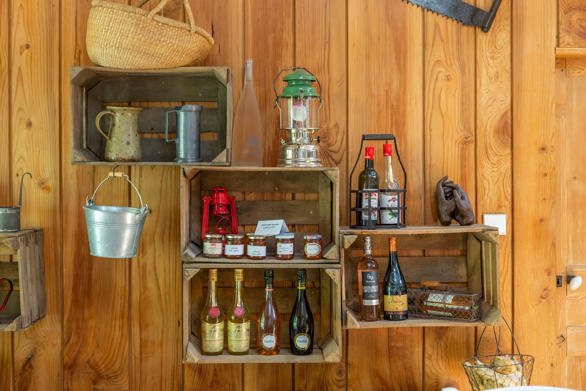 Caisses de bois fixées au mur lambrissé avec pots de confiture, vins, lampes tempête et seau en zinc
