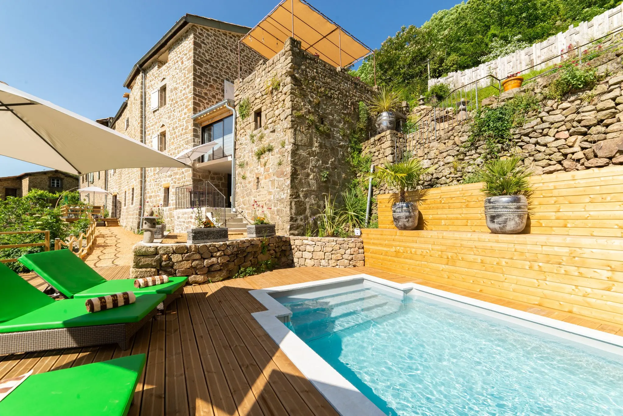 Maison en pierre étagée sur des restanques, piscine et terrasse en bois au premier plan