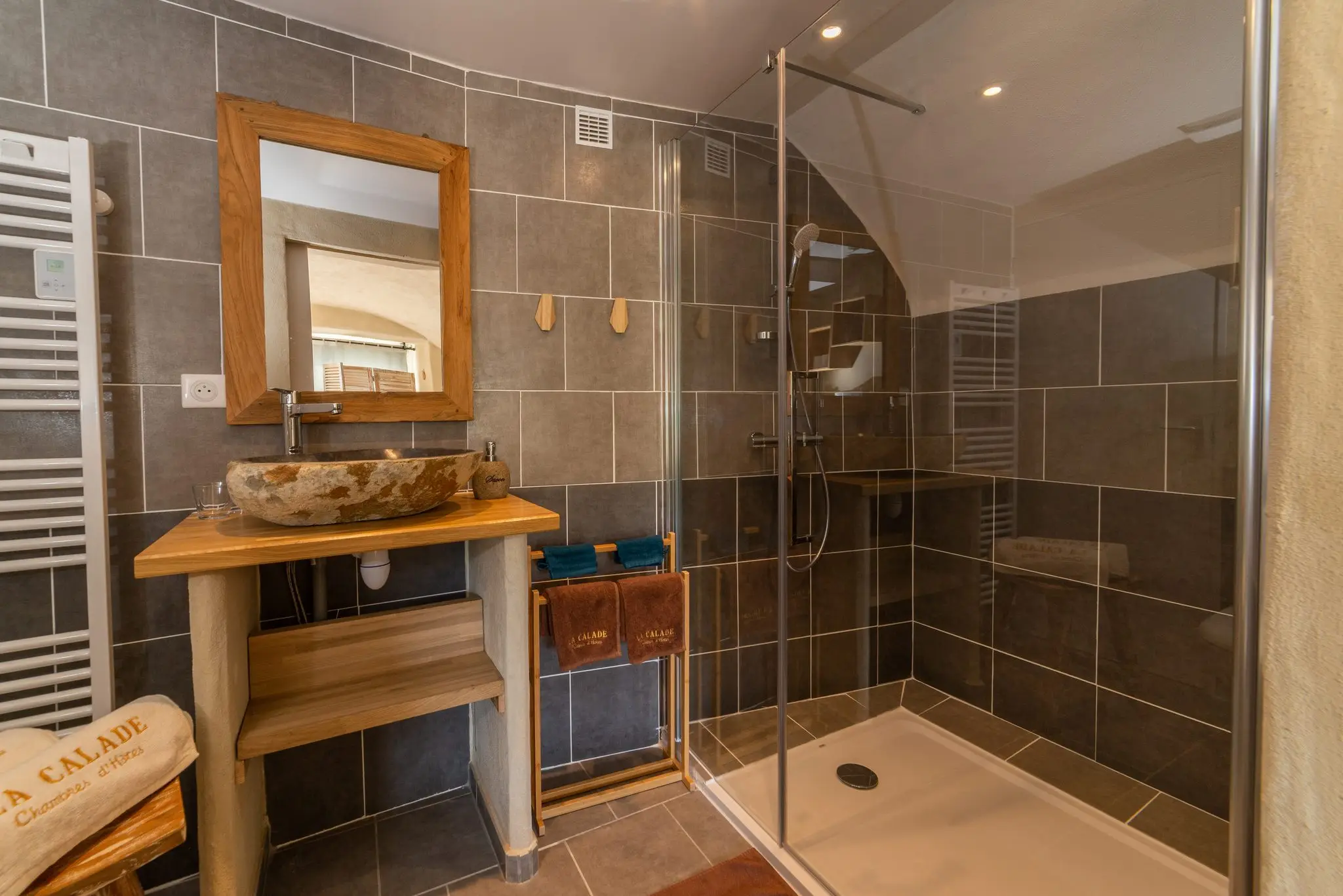 Salle de douche en carrelage gris, vasque en pierre posée sur un meuble en bois