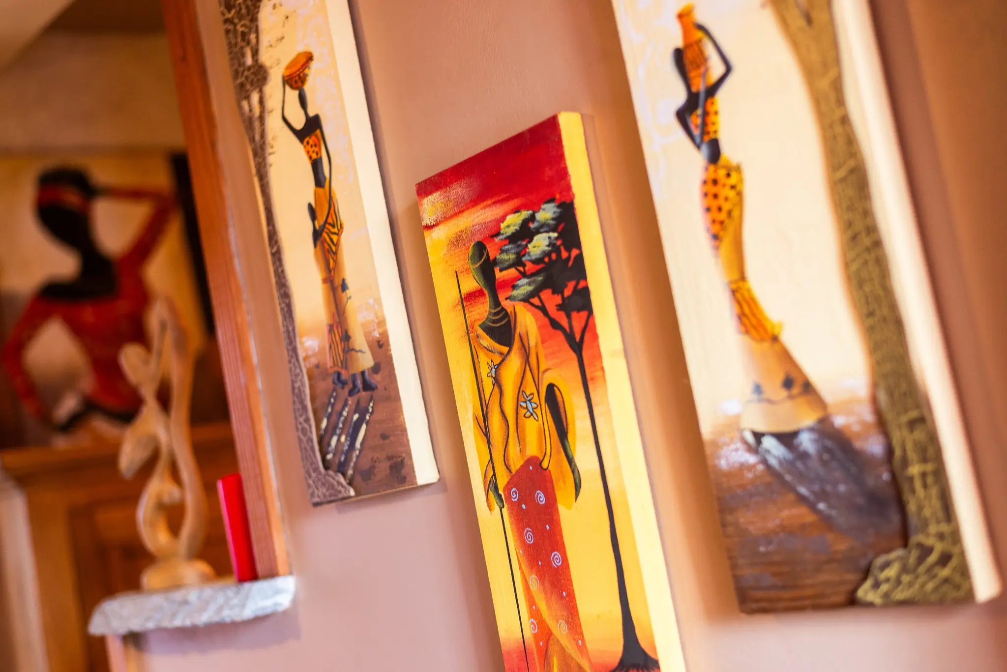 Trois tableaux aux tons chauds représentant des silhouettes féminines accrochés sur un mur rose