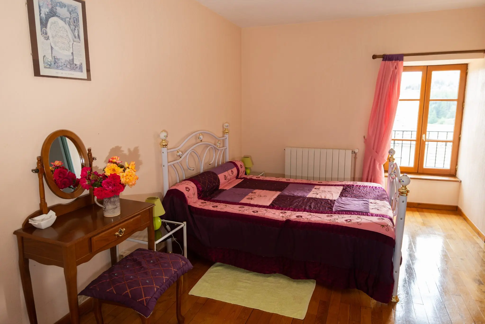 Chambre aux murs pêche, lit en fer forgé et couvre-lit patchwork mauve, coiffeuse à miroir ovale et fenêtre à rideau rose