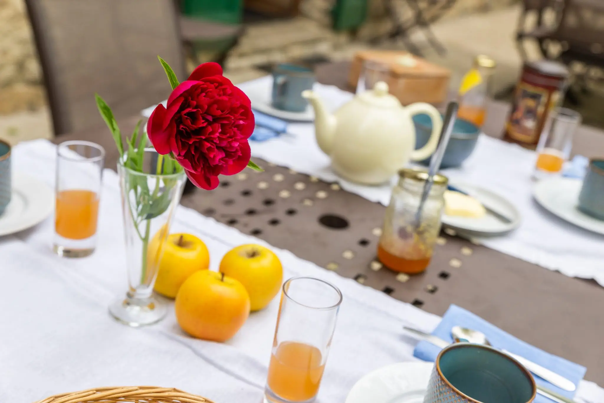 Pivoine rouge dans un verre, pommes jaunes, jus d'orange et théière sur la table du petit-déjeuner