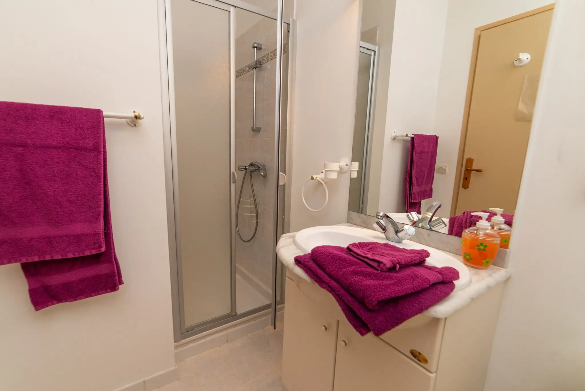 Salle d'eau blanche avec cabine de douche vitrée, vasque et serviettes prune pliées