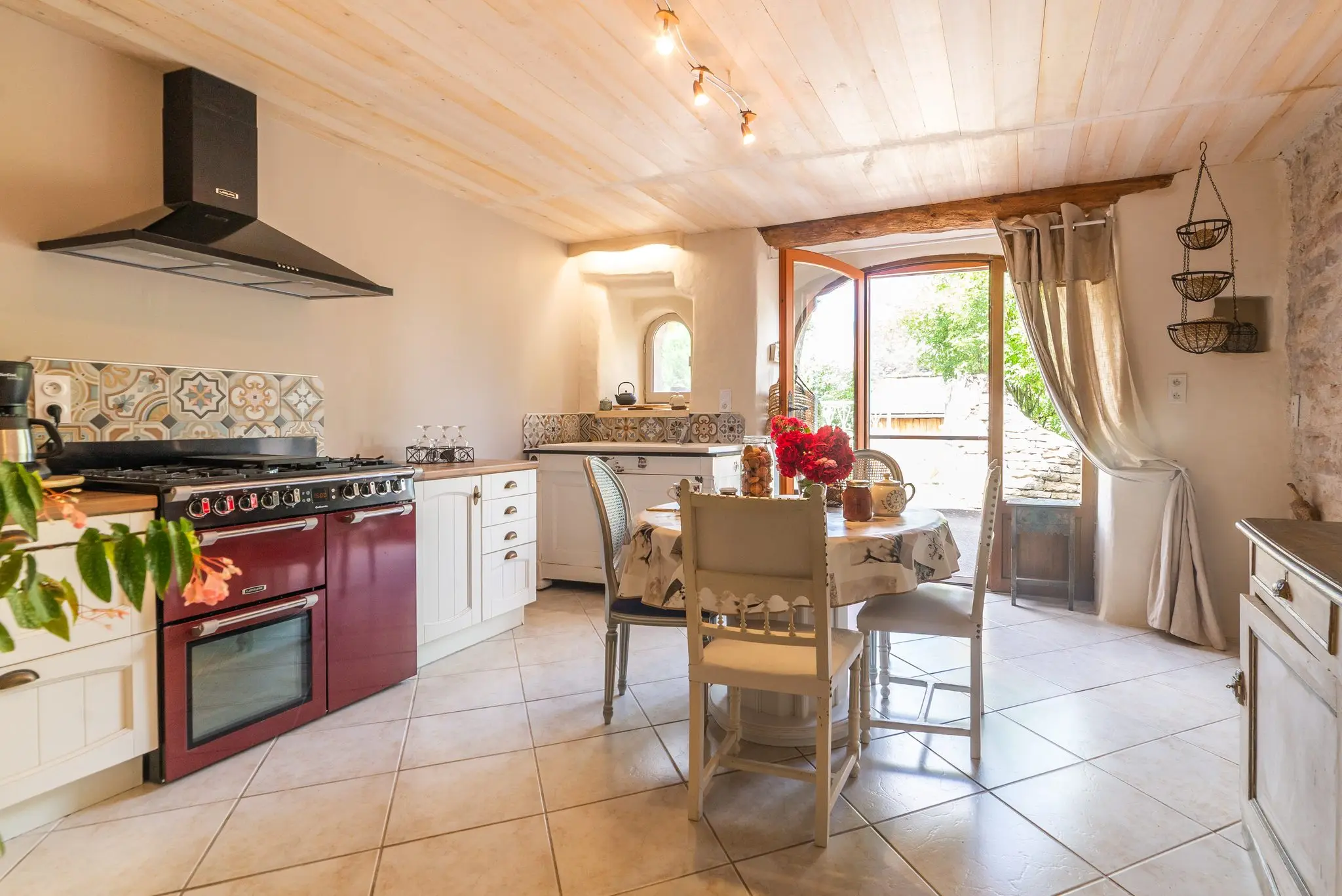 Cuisine d'un gîte en Lozère, piano de cuisson bordeaux, crédence en carreaux de ciment et porte-fenêtre
