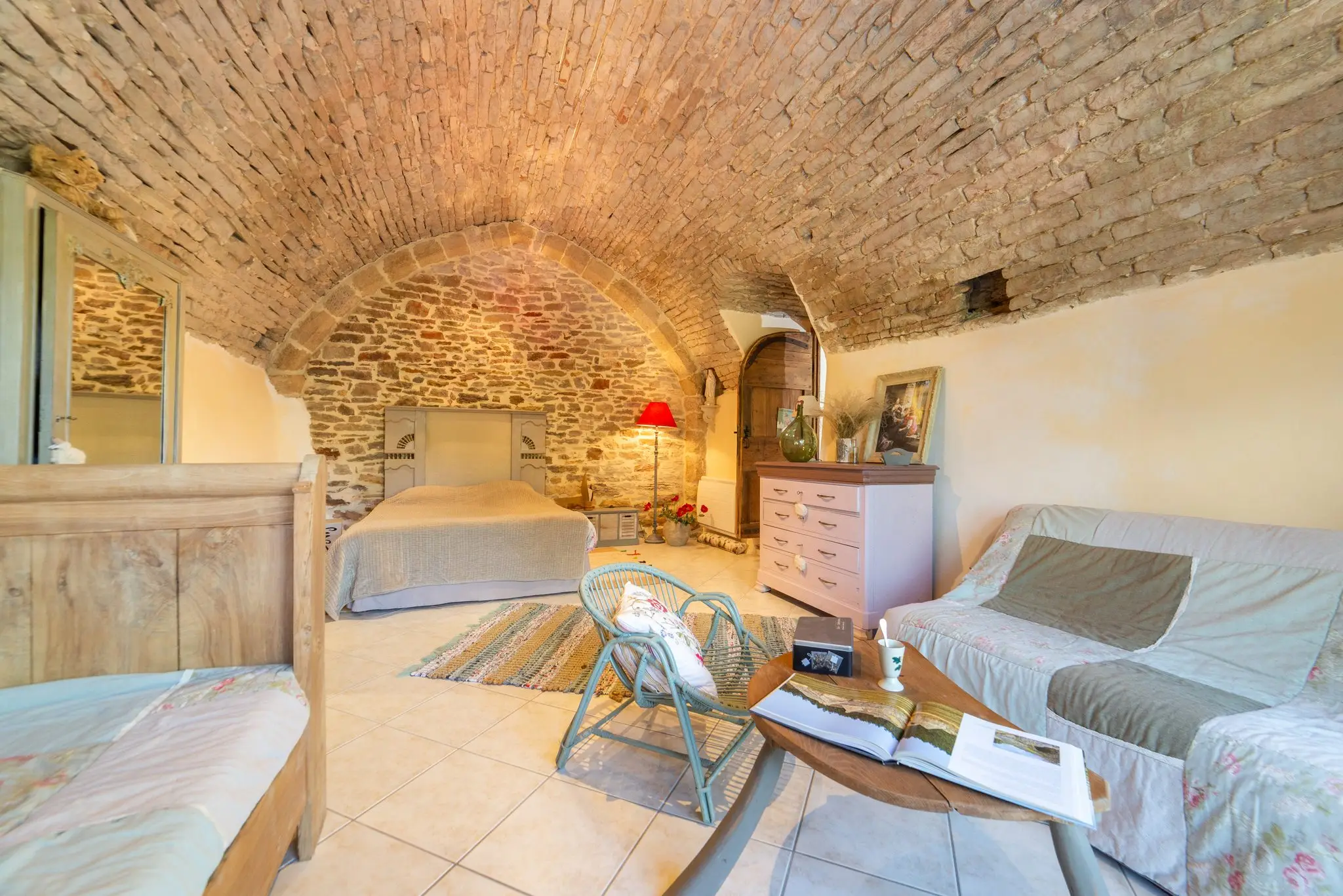 Vaste chambre sous voûte en pierre, lit double sous l'arc, canapé, commode rose et table basse en bois
