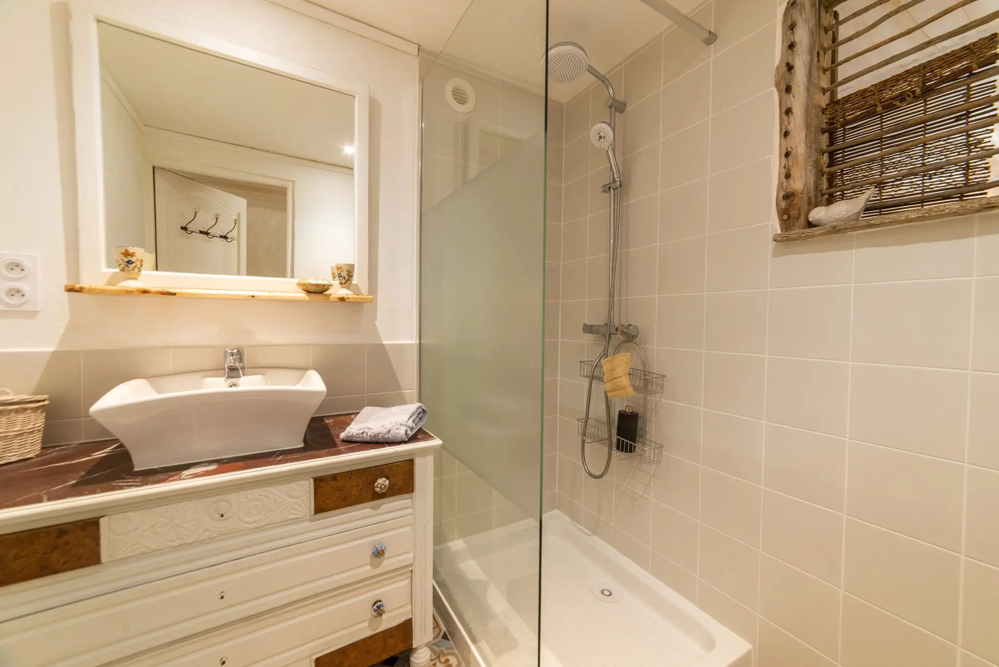 Salle d'eau claire, vasque posée sur une commode ancienne, douche vitrée et petite fenêtre à store en bambou