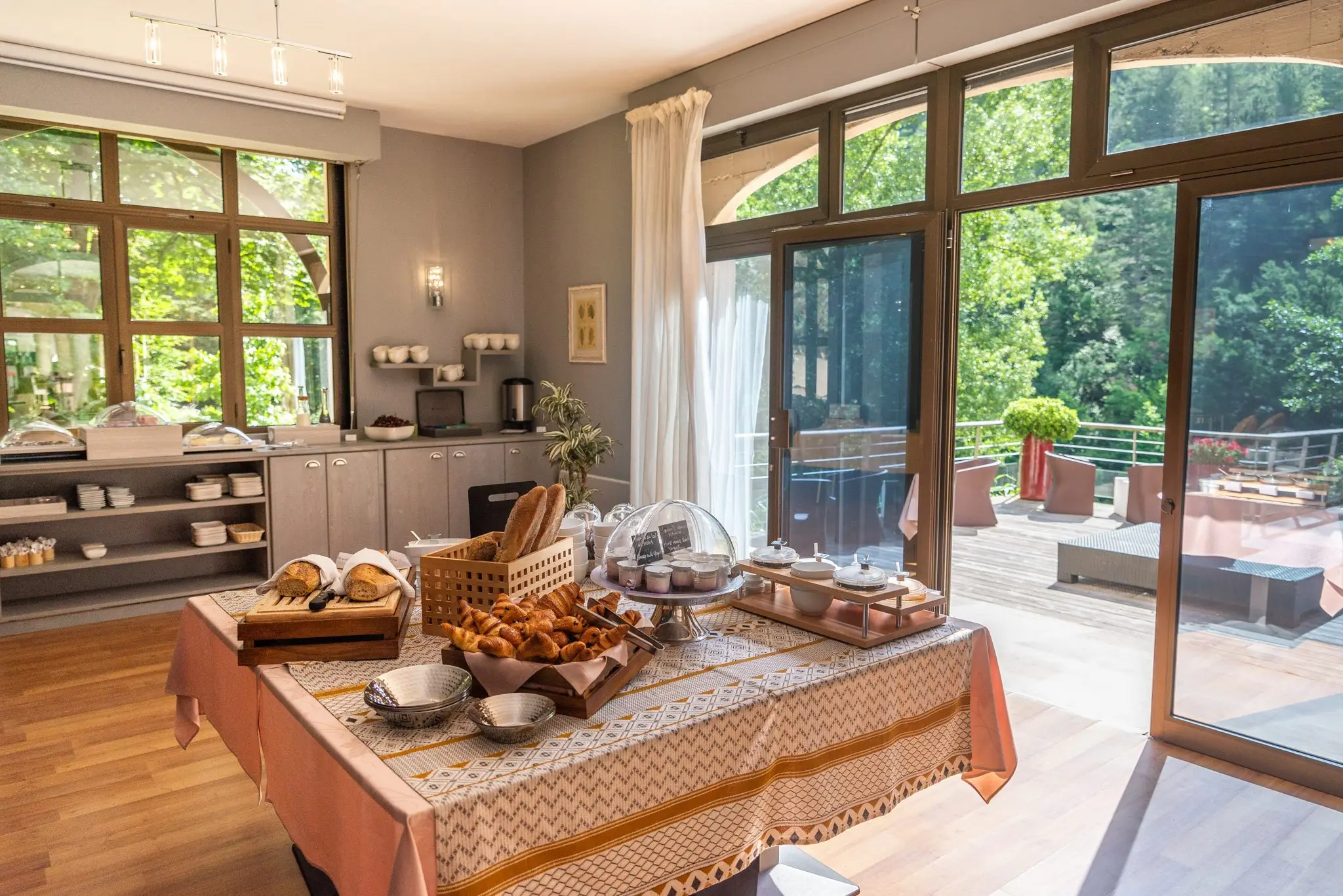 Buffet du petit-déjeuner d'un hôtel, baies vitrées ouvertes sur la terrasse et la forêt