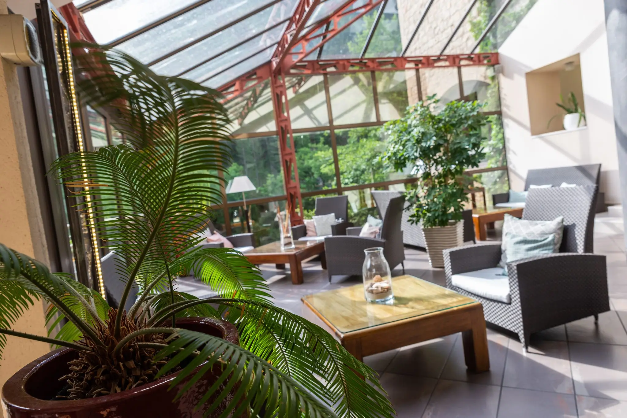 Salon sous verrière d'un hôtel des gorges du Tarn, fauteuils tressés, tables basses et plantes vertes
