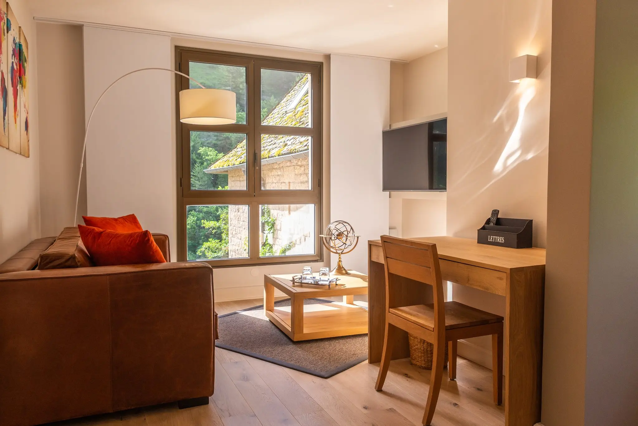 Coin salon d'une suite d'hôtel avec canapé en cuir, bureau en bois et fenêtre sur les maisons de pierre