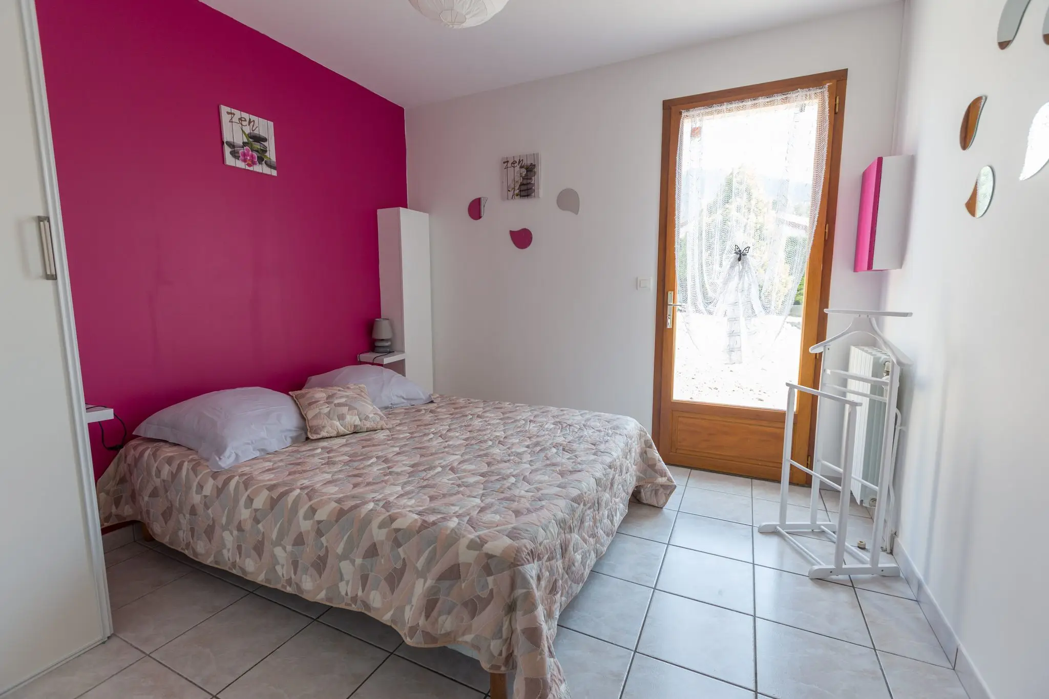 Chambre au mur framboise, lit double au couvre-lit à motifs, porte-fenêtre vitrée donnant sur l'extérieur