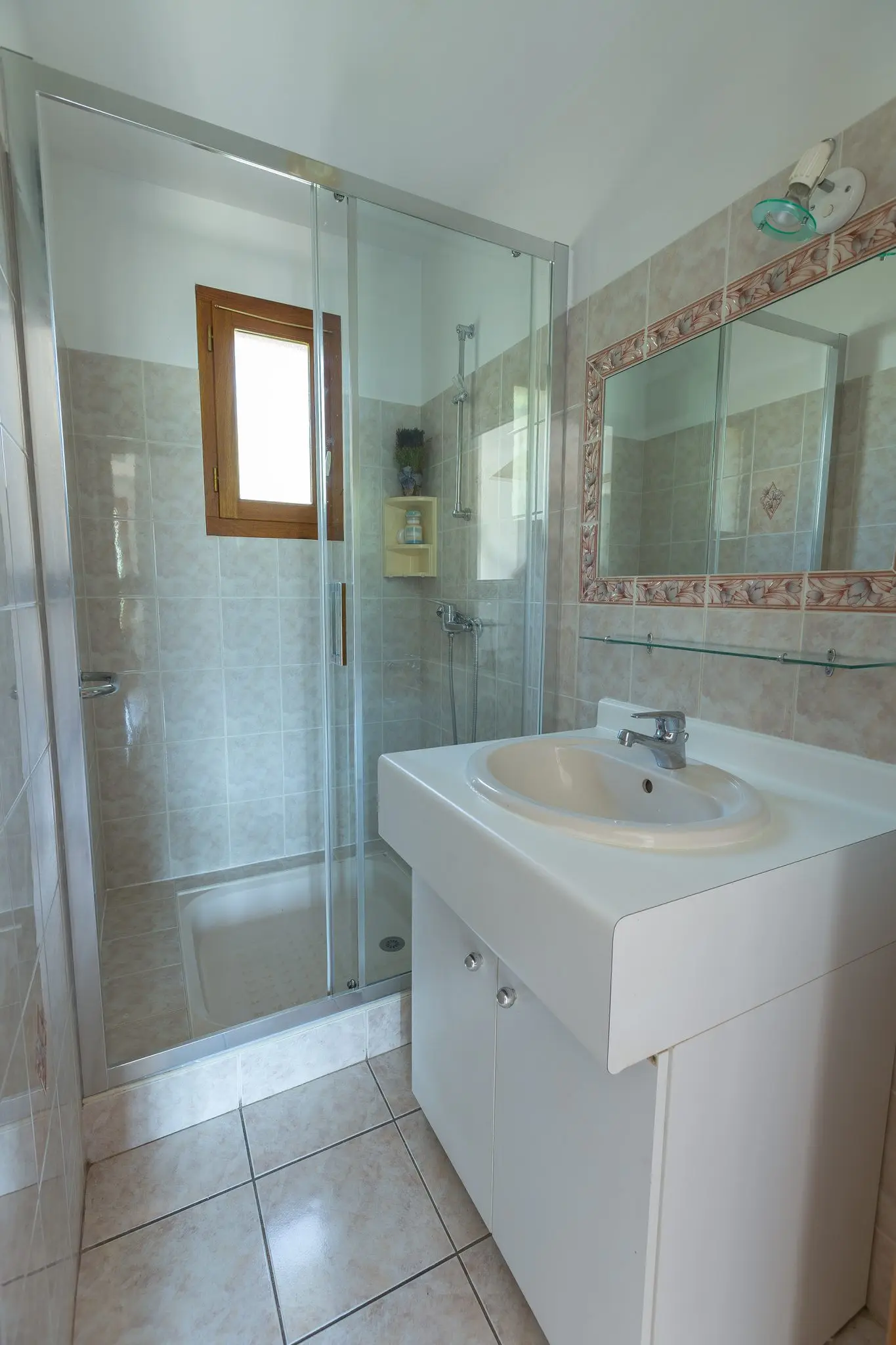 Salle d'eau carrelée, douche à parois vitrées, meuble vasque blanc et miroir