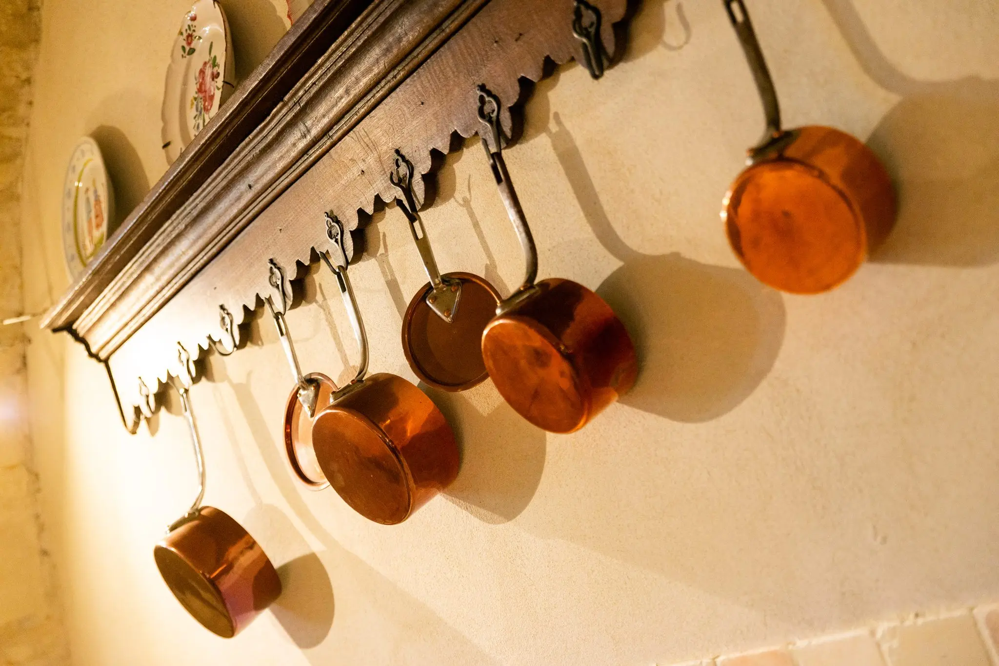 Casseroles en cuivre suspendues à une étagère en bois ancienne, sur le mur blanc de la cuisine
