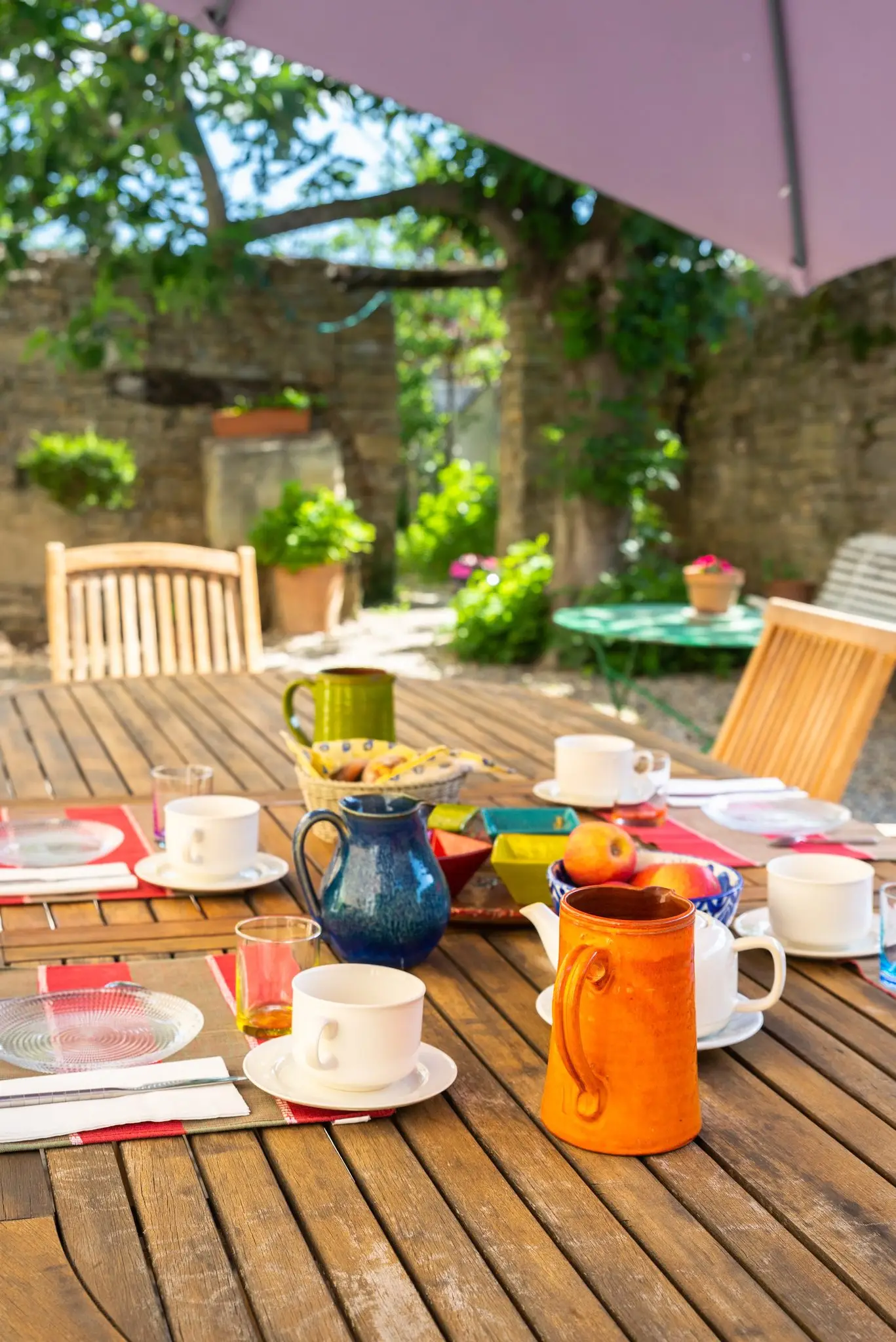 Petit-déjeuner servi dans une cour en pierre, céramiques colorées et pommes sur une table en bois