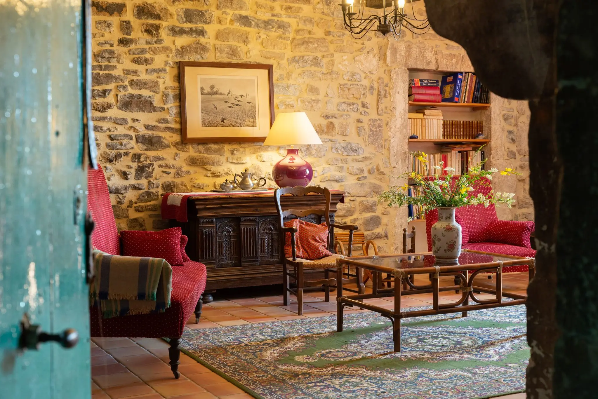 Salon aux murs de pierre d'une maison d'hôtes, fauteuils rouges, lampe et bibliothèque