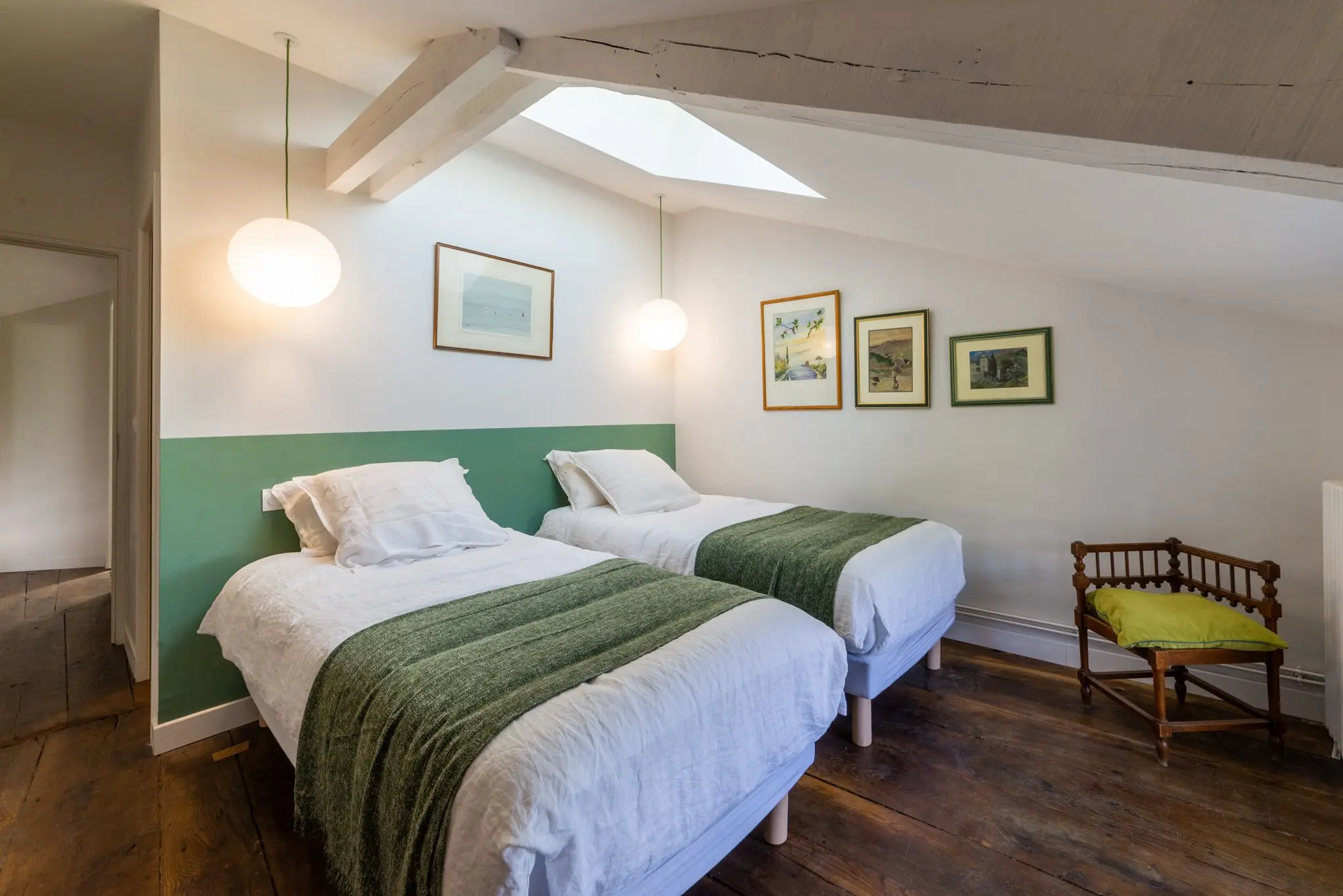 Chambre mansardée aux deux lits jumeaux, jetés verts, soubassement vert et fenêtre de toit