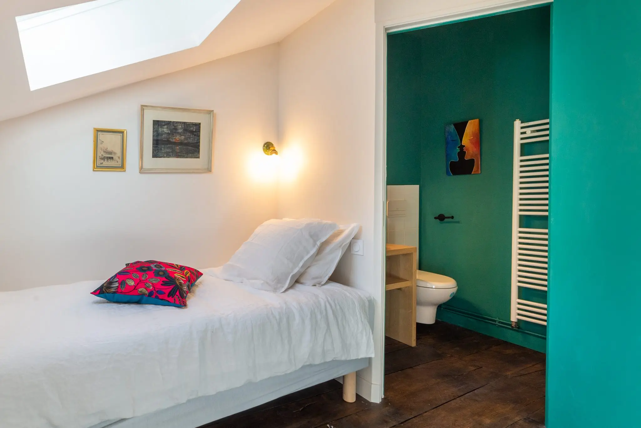 Lit double blanc à coussin fuchsia, ouverture sur une salle d'eau aux murs vert émeraude
