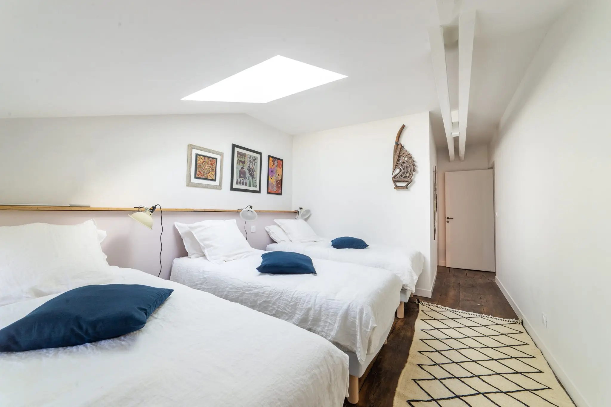 Chambre d'hôtes lumineuse à trois lits simples, poutres blanches et fenêtre de toit