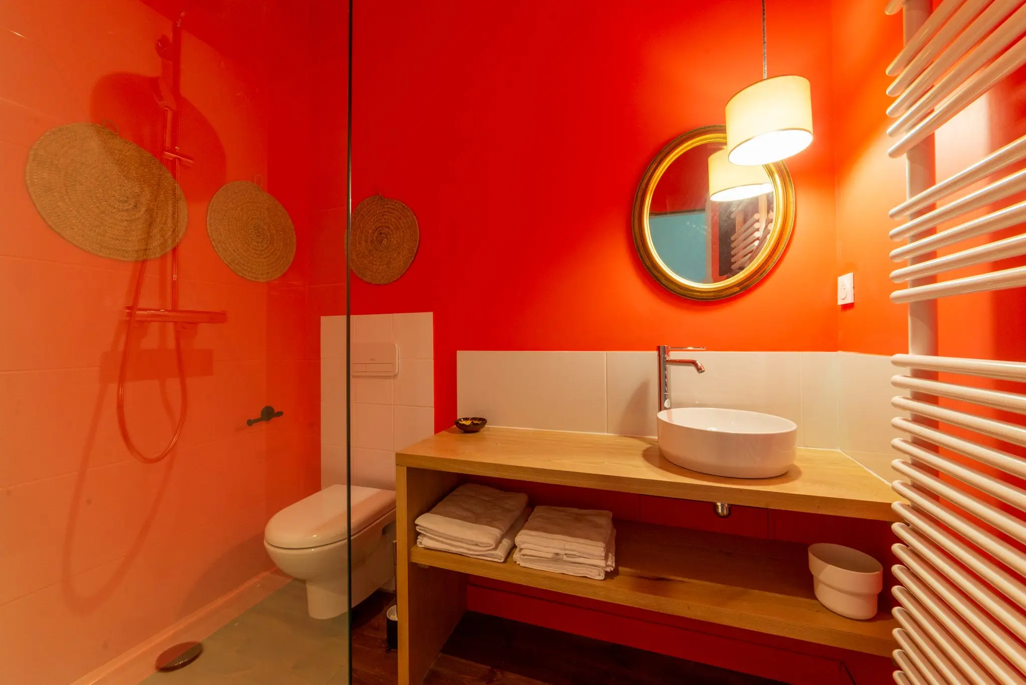 Salle d'eau au mur rouge vif, vasque posée sur un meuble en bois, douche vitrée et sèche-serviettes