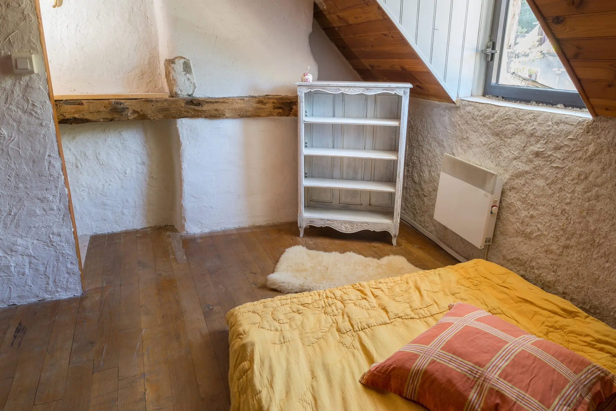 Chambre sous rampant lambrissé, murs blanchis, parquet ancien, petite étagère blanche et lit au couvre-lit jaune