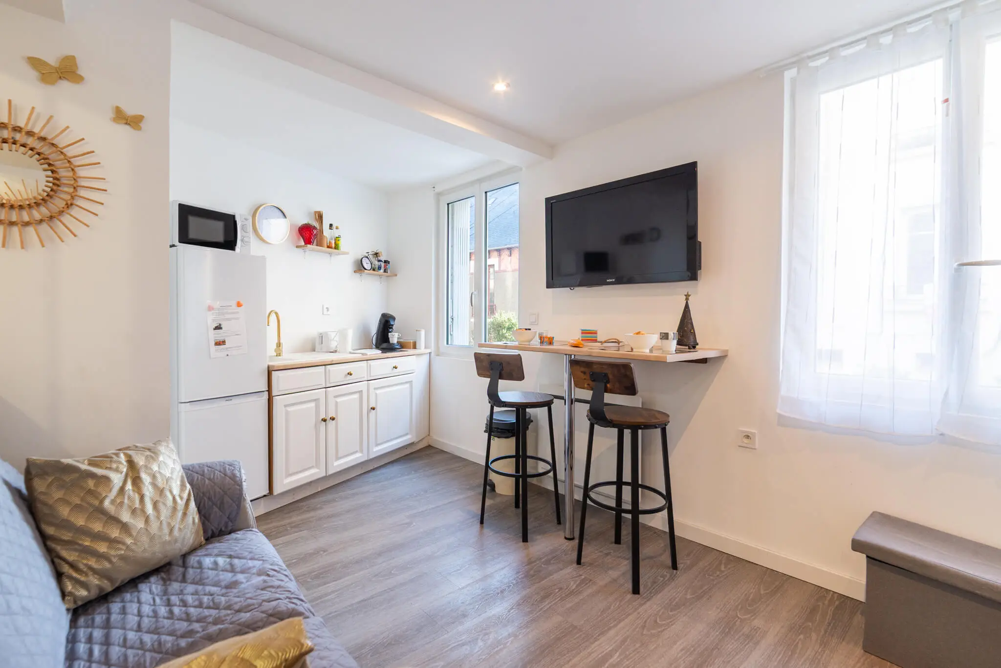 Studio meublé à Rodez, coin cuisine blanc, bar avec deux tabourets et canapé, lumière naturelle