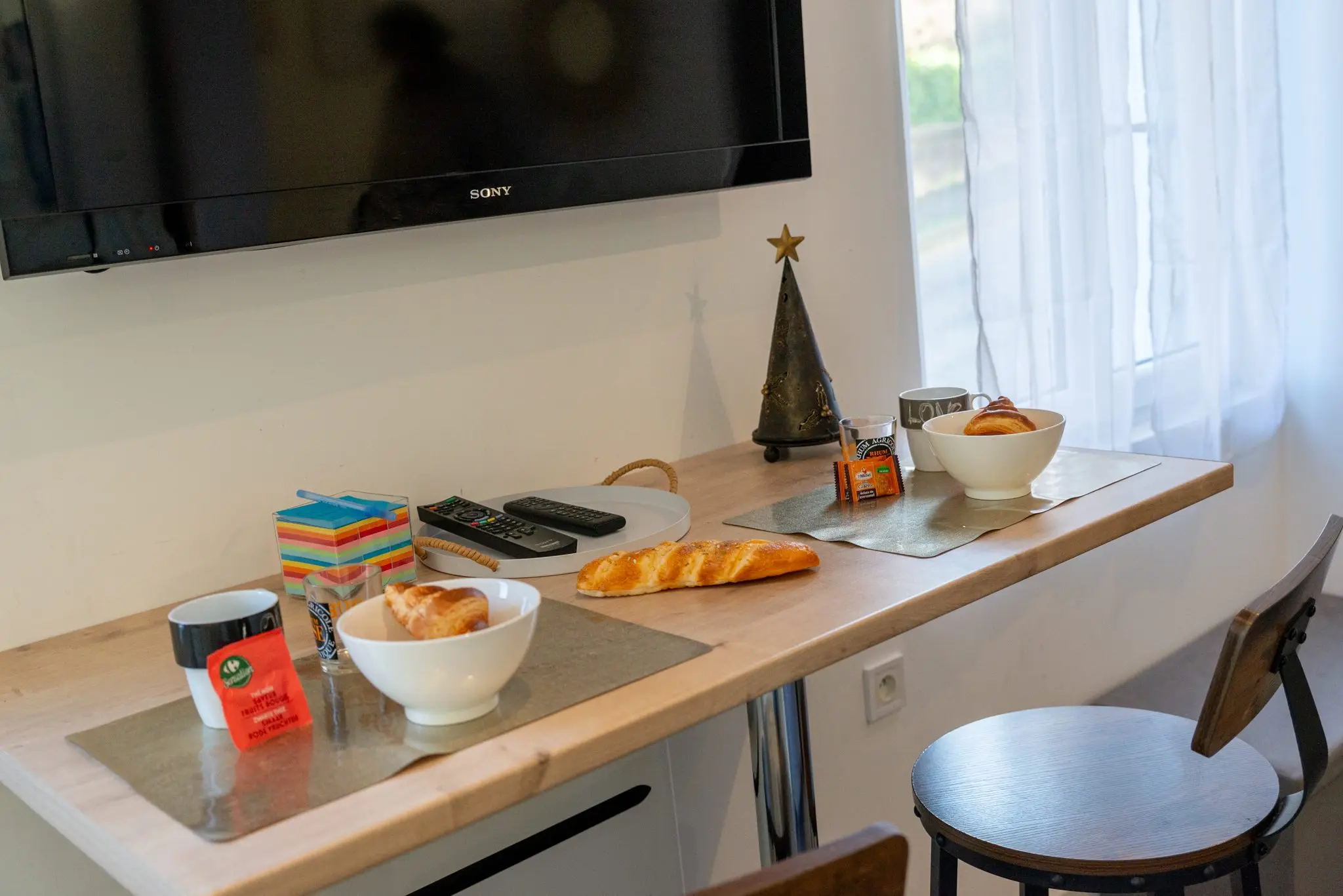 Bar en bois dressé pour le petit-déjeuner, bols, viennoiseries et tabouret, sous la télévision murale