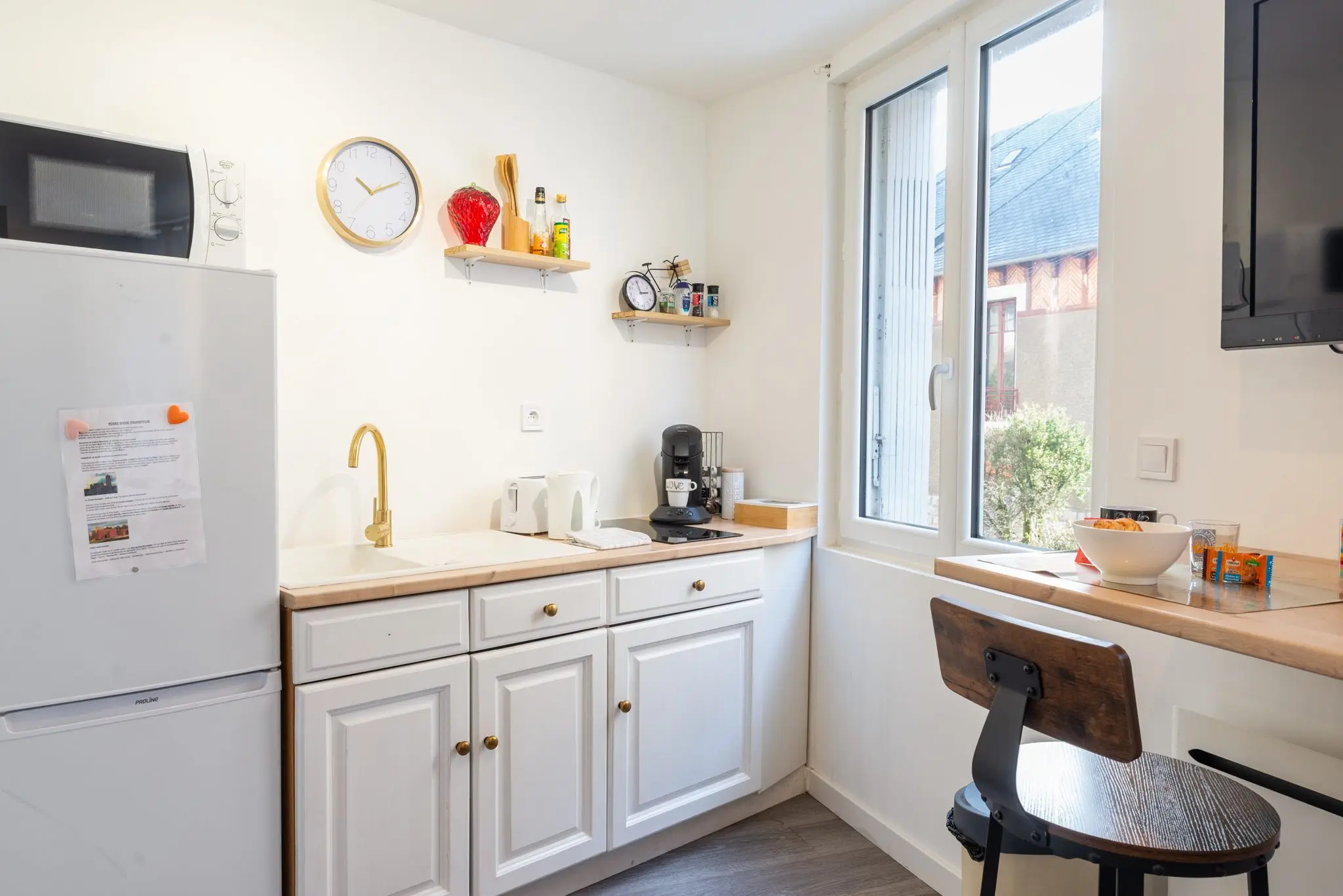 Coin cuisine blanc avec évier, robinet doré et machine à café, à côté d'une fenêtre