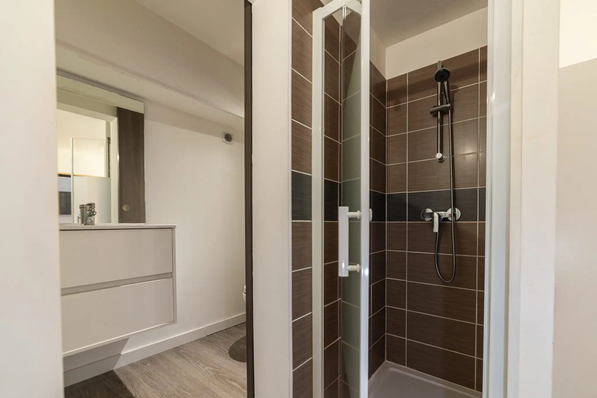 Salle d'eau avec meuble vasque blanc et douche carrelée à porte vitrée