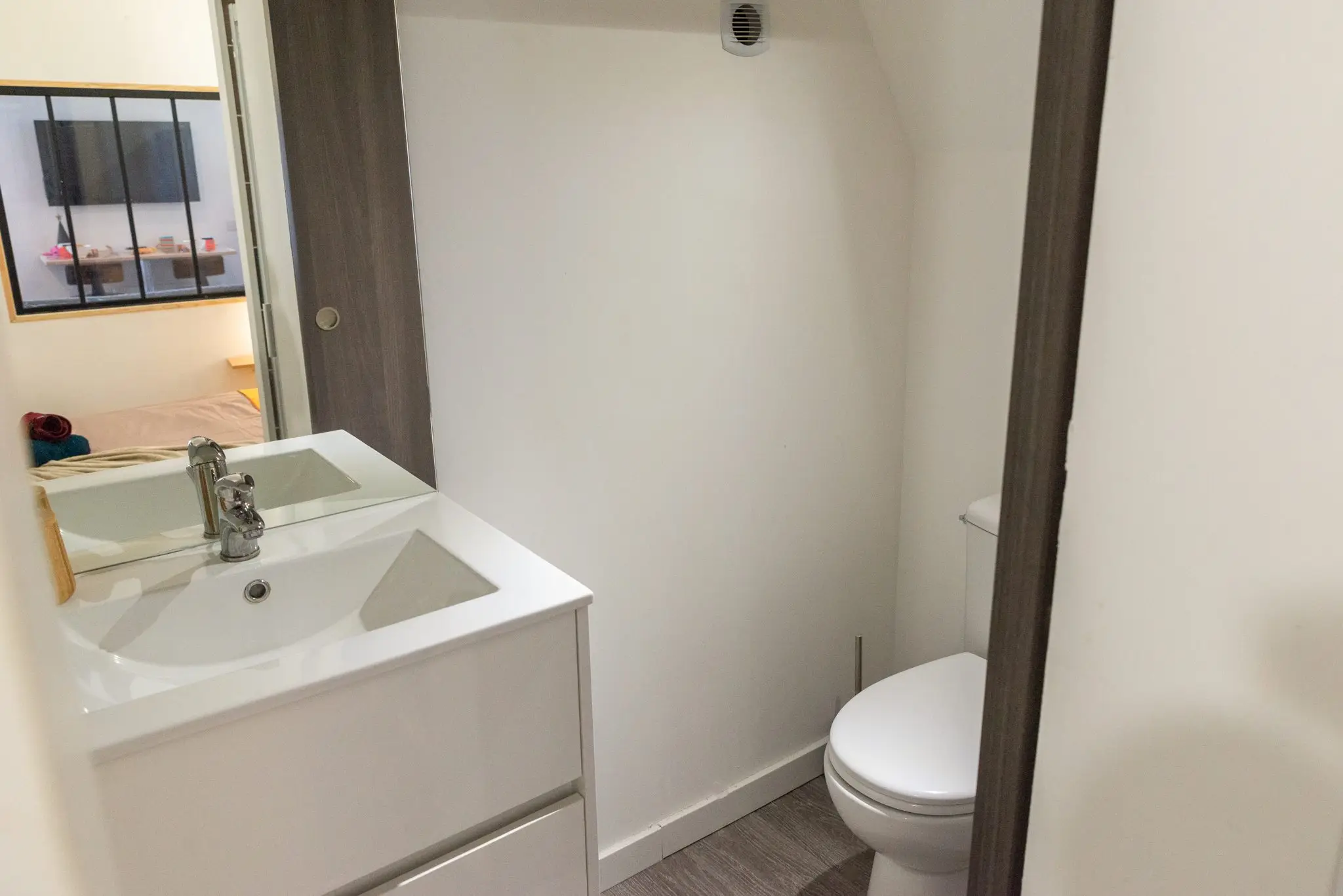 Meuble vasque blanc, miroir et WC dans une salle d'eau aux murs blancs