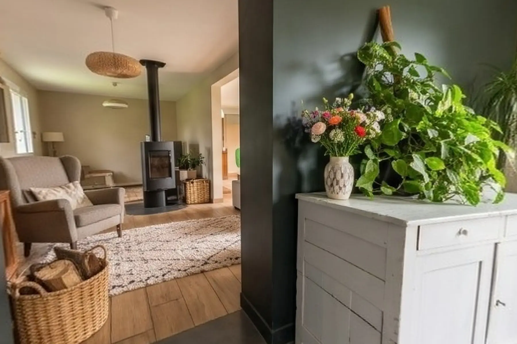 Entrée au carrelage gris et mur vert foncé, buffet blanc fleuri, ouverte sur le séjour et son poêle à bois